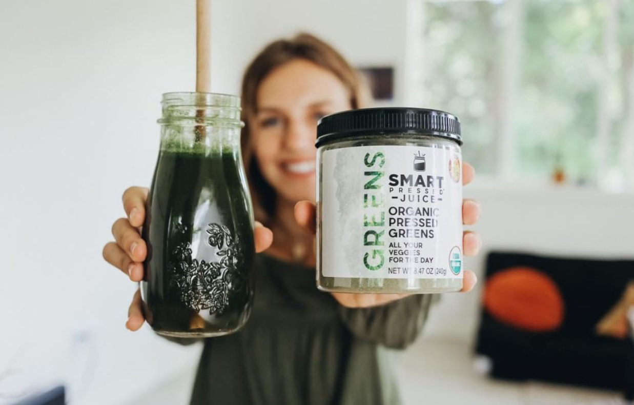 a mason jar filled with smart pressed organic green juice and a jar of smart labeled green organic juice holding by a woman