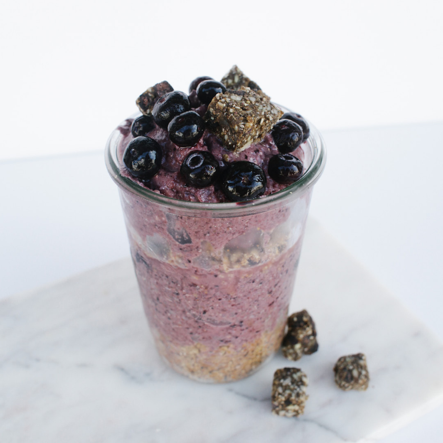 a cup of superfood protein smoothie topped with blueberries and frozen black acai with three blocks of frozen acai on the side on top of a marble table